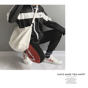 Street style shot of large white canvas messenger bag with contrast stripe sports pants