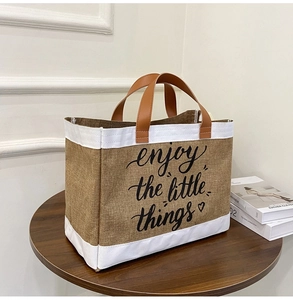 Detail of jute tote bag with brown leather handles and 'enjoy the little things' print