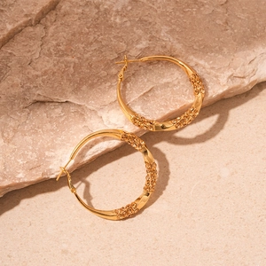 Close-up of golden geometric twisted hoop earrings with champagne diamonds on a stone surface