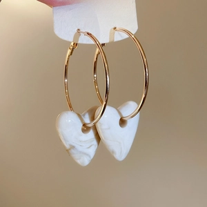 Macro view of gold hoop earrings featuring white marble heart-shaped resin pendants