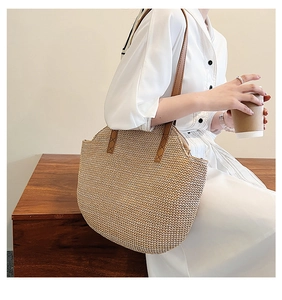Detail of handwoven beige straw tote with reinforced brown leather straps and stitching