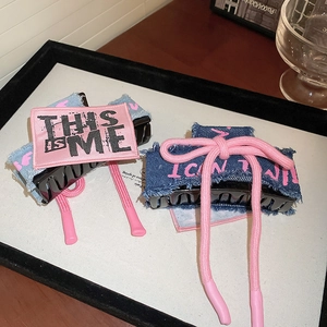 Close-up of denim bow hair claws with pink embroidery and rope detail on a display stand