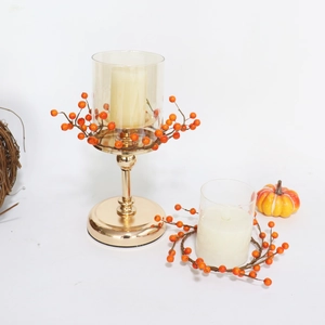 Detail von goldenem Kerzenhalter-Set mit orangefarbenen Beerenringen und Kürbis