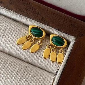 Dettaglio di orecchini vintage in oro con pietre di malachite e nappe a goccia su lino