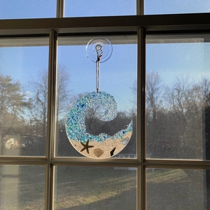 Detail of beach suncatcher with crushed blue sea glass wave, real sand and tiny starfish