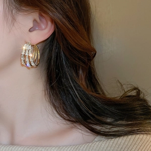 Gros plan de boucles d'oreilles dorées à trois rangées avec cristaux carrés au look luxueux