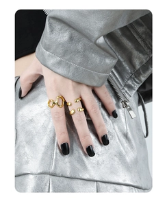 Close-up of golden irregular geometric hollow rings worn by a model on a metallic jacket