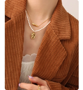 Close-up of layered 18K gold snake chain and pearl necklace with oval pendant
