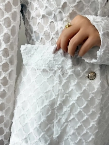 Close-up of white textured jacquard fabric and embossed golden lion head button