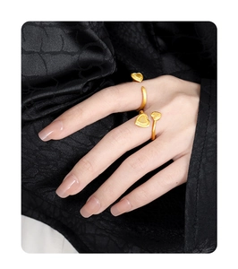 Detail of matte gold heart rings on model's hand over black silk background