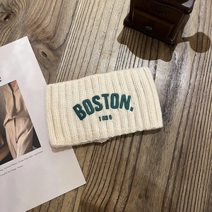 Détail du bandeau en maille crème avec broderie Boston sur une surface en bois