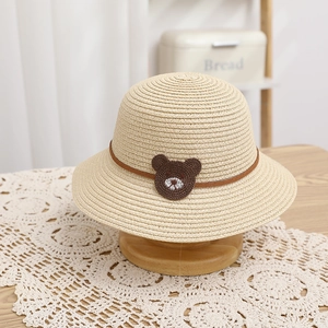 Detailed close-up of straw sun hat featuring a cute brown bear patch and leather strap