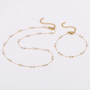 Close-up of a gold chain necklace and bracelet set with white beads on white background