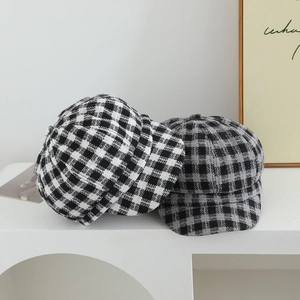 Close-up of black and white plaid wool newsboy caps on a minimalist white stand