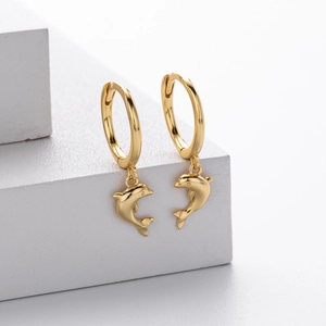 Close-up of golden dolphin charms on small hoop earrings on a white display pedestal