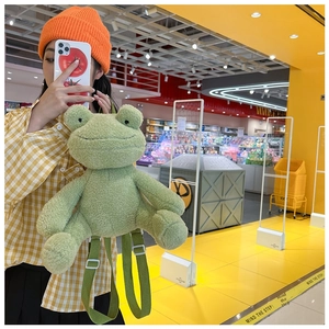Detail of green plush frog backpack with soft texture and adjustable straps worn by model