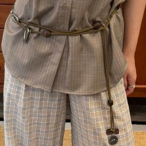 Detail view of woven olive green tasseled waist belt styled on plaid vintage clothing