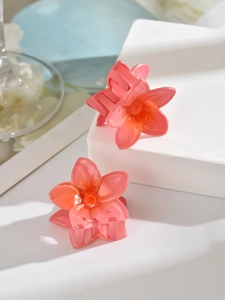 Detail of two translucent coral pink flower hair claws with orange center on stone background