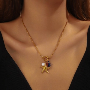Gold beaded necklace with starfish, pearl, red bead and blue tassel charms on a model
