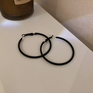 Detail showing a pair of minimalist matte black hoop earrings on white background
