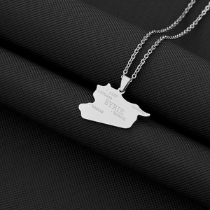 Detailed close-up of silver Syria map pendant with engraved city names on black fabric