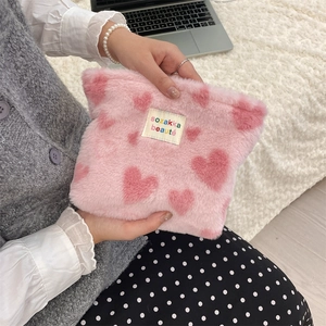 Pink plush cosmetics bag with red heart patterns held in hands in a cozy home setting