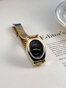 Detail of elegant gold watch with black oval dial placed on a magazine page