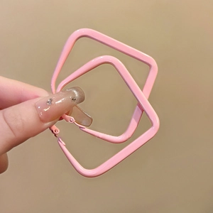 Detail showing hand holding interlocking pink square earrings in a minimalist metal design