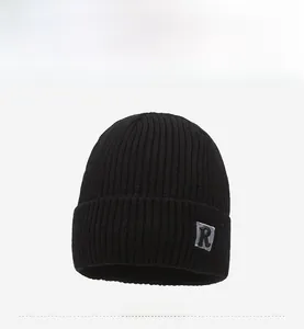 Close-up of black ribbed knit beanie featuring a grey square patch with a bold R letter