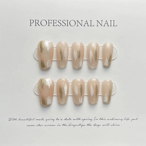 Artistic press-on nails with nude pink base, white brush strokes, and gold foil details