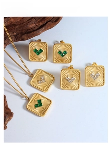 Detail of gold jewelry set featuring square pendants with sunburst texture and green gems