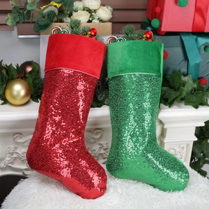Large red and green sequined Christmas stockings on white fur mat near fireplace