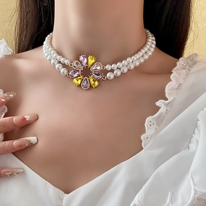 Detail einer zweireihigen Perlenkette mit einem lila-gelben Kristallblumenanhänger
