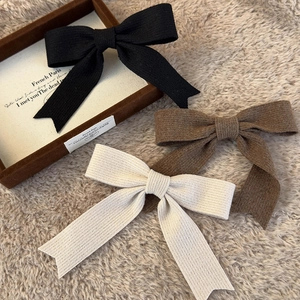 Close-up of three knitted bow hair clips in black, brown and beige with ribbed texture