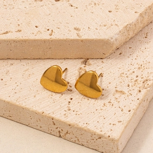 Detailed close-up of golden heart stud earrings on elegant beige stone blocks