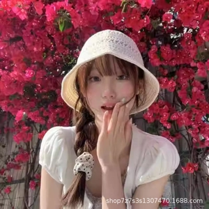 Outdoor shot of a woman wearing a white crochet bucket hat against red floral background