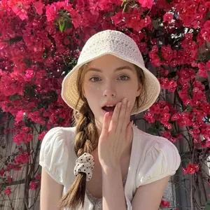 Outdoor shot of a woman wearing a white crochet bucket hat against red floral background