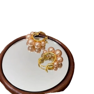 Gold-plated C-shaped earrings with pink gradient pearls on a reflective mirror surface