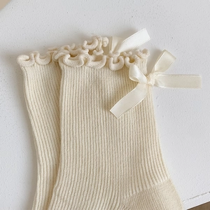 Detail of cream rib knit socks with ruffled edges and silk ribbon bow embellishment