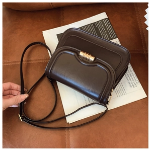 Détail d'un sac besace marron foncé vintage avec fermoir doré sur fond de journal rétro