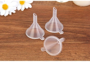 Three transparent plastic mini funnels for perfume and cosmetics on a wooden background