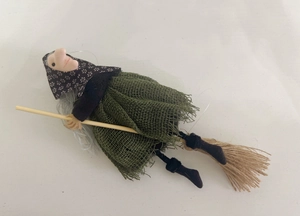 Macro detail of a handmade Halloween witch doll riding a wooden broomstick pendant