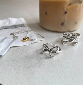 Detail of 925 sterling silver bow ring and layered band with gold letter bracelet