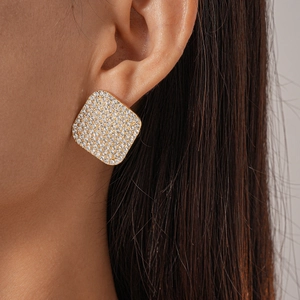 Close-up of golden square stud earrings with pave-set diamonds on a female model