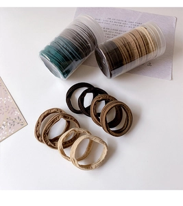 Detail view of high-elasticity nylon hair ties in earth tones with cylinder packaging