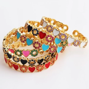 Macro detail of gold-plated open bangles featuring colorful heart enamel and zircons