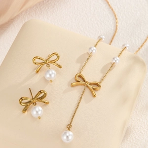 Elegant gold bow necklace and pearl earring set displayed on a soft jewelry stand
