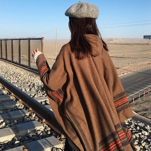 Ethnic striped knit poncho with fringe and hood shown in a scenic outdoor desert landscape