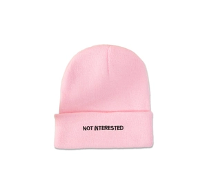 Close-up of NOT INTERESTED black embroidery on a pink cuffed winter beanie hat