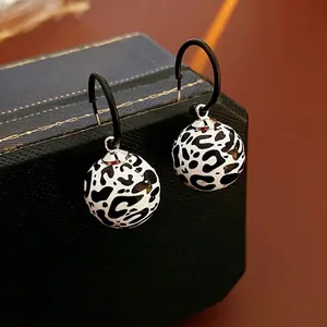 Modern leopard print ball earrings with black hoop hooks and a minimalist luxury style